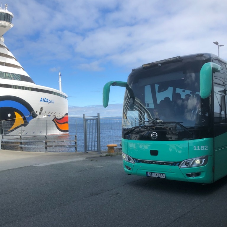 Nærbilde av front på cruiseskip og buss som ligger tett ved hverandre på havna