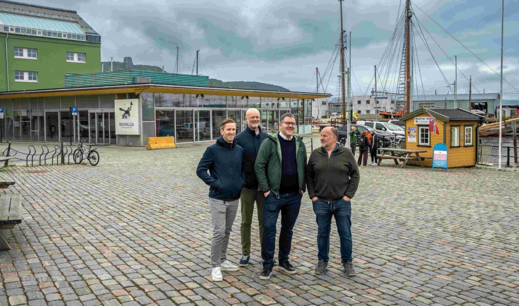Fire menn poserer foran bygning i havneområde