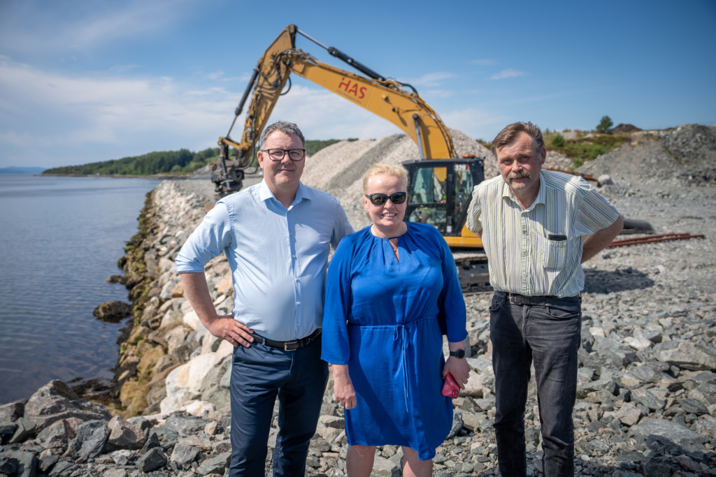 Mennesker foran gravemaskin smiler til kamera.